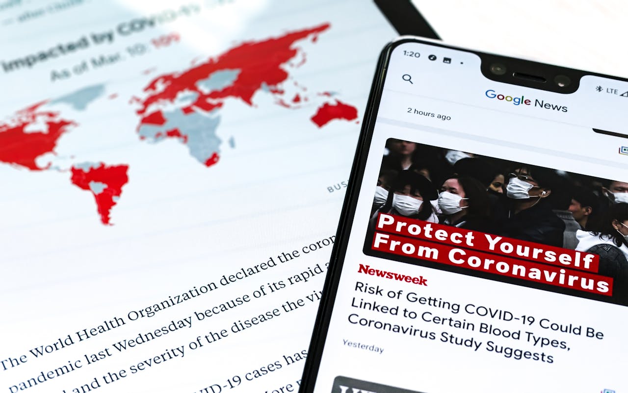 hero-img-01 Smartphone with coronavirus updates and world map showing the impact of COVID-19.