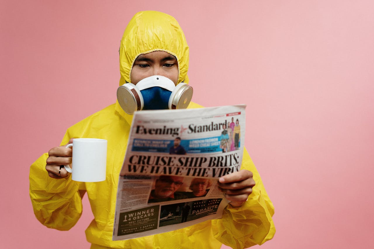 services-02 Person in yellow protective suit reading a newspaper with a mug.